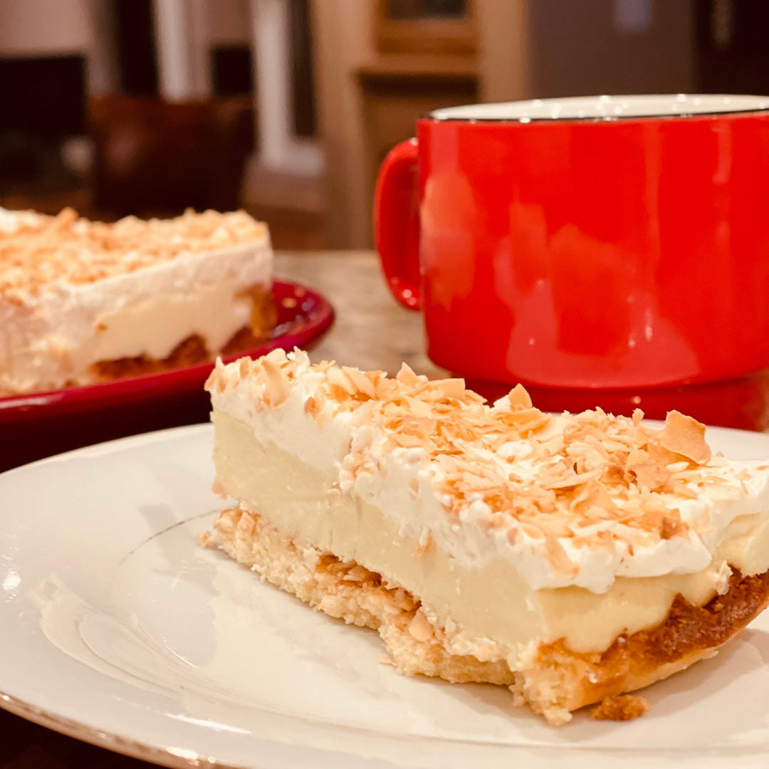 no bake Allulose based keto Coconut Cream Pie slice is on a plate and a red coffee cup next to it